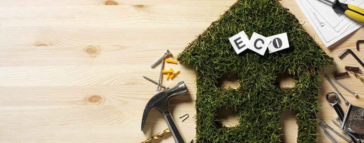 Eco house cut out of grass with construction tools on a wooden background. Copy space